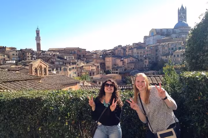 Two women posing with peace signs in front of Siena's historic skyline during a Tuscany day trip from Rome.