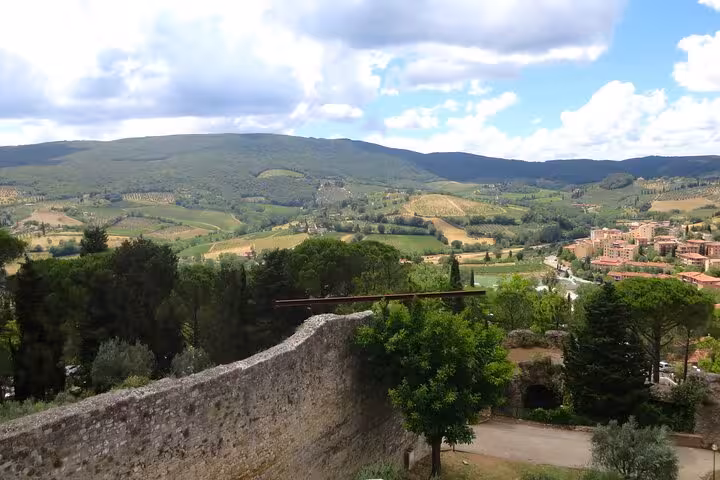Panoramic view of Tuscany's rolling hills and vineyards under a cloudy sky.
