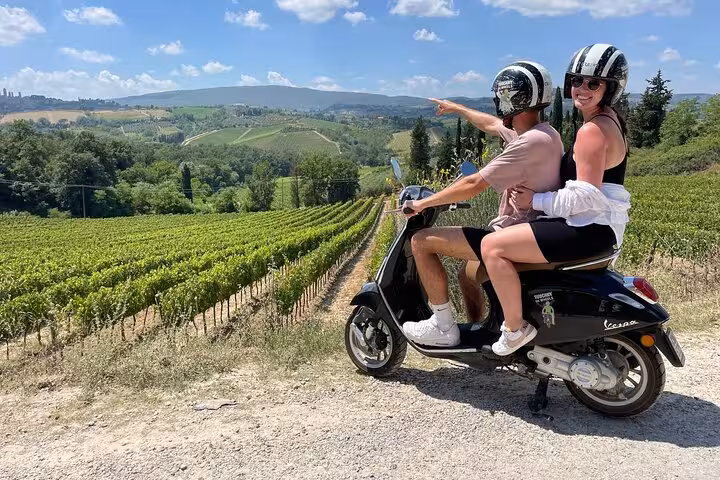 Couple enjoying Tuscany Vespa tour overlooking lush vineyards under a sunny sky.