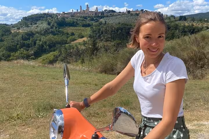 Discover Tuscany's scenic beauty on a Vespa tour with a view of San Gimignano's skyline in the background.