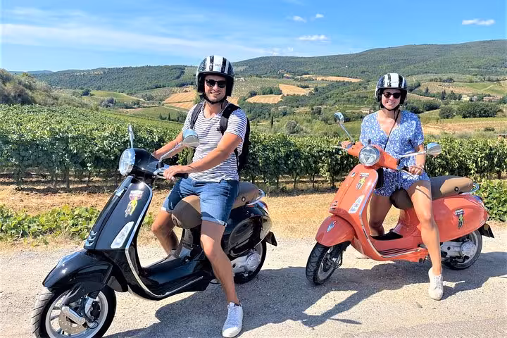 Two riders on Vespas exploring Tuscany's picturesque vineyards under clear blue skies.