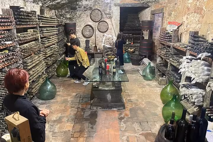 Visitors exploring a rustic wine cellar in Tuscany, surrounded by vintage bottles and historic charm.