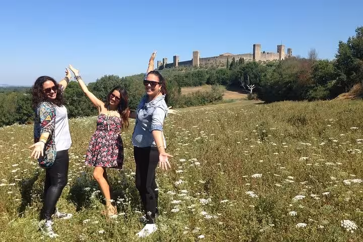 Three friends pose joyfully in a wildflower field with the medieval walls of Monteriggioni in the background in Tuscany.
