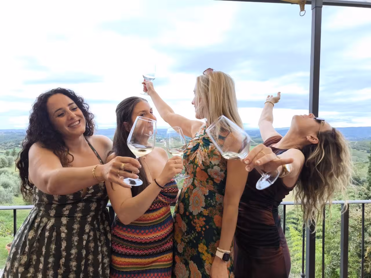 Four friends celebrating with wine glasses on a Tuscany balcony, overlooking lush vineyards on a private tour.
