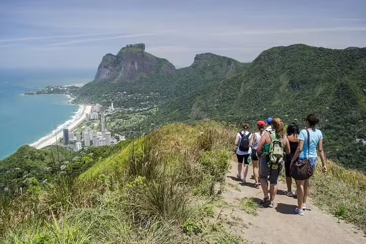 Group of hikers trekking along a scenic trail overlooking Two Brothers Hill and Rio's coastline.