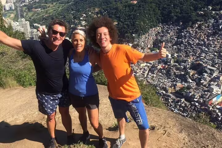 Group of friends celebrates reaching the summit of Two Brothers Hill with panoramic views of Vidigal Favela below.