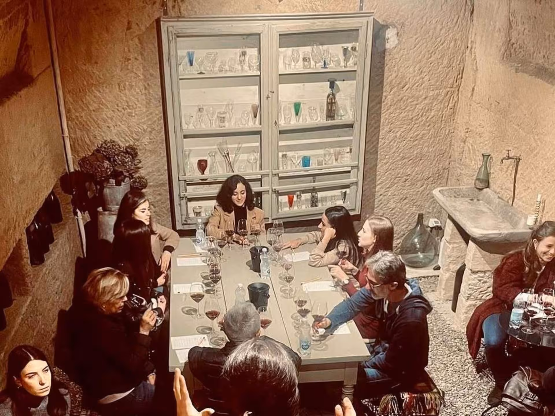 Visitors savoring wine and conversation in an underground cave near Asti, with elegant glassware display.
