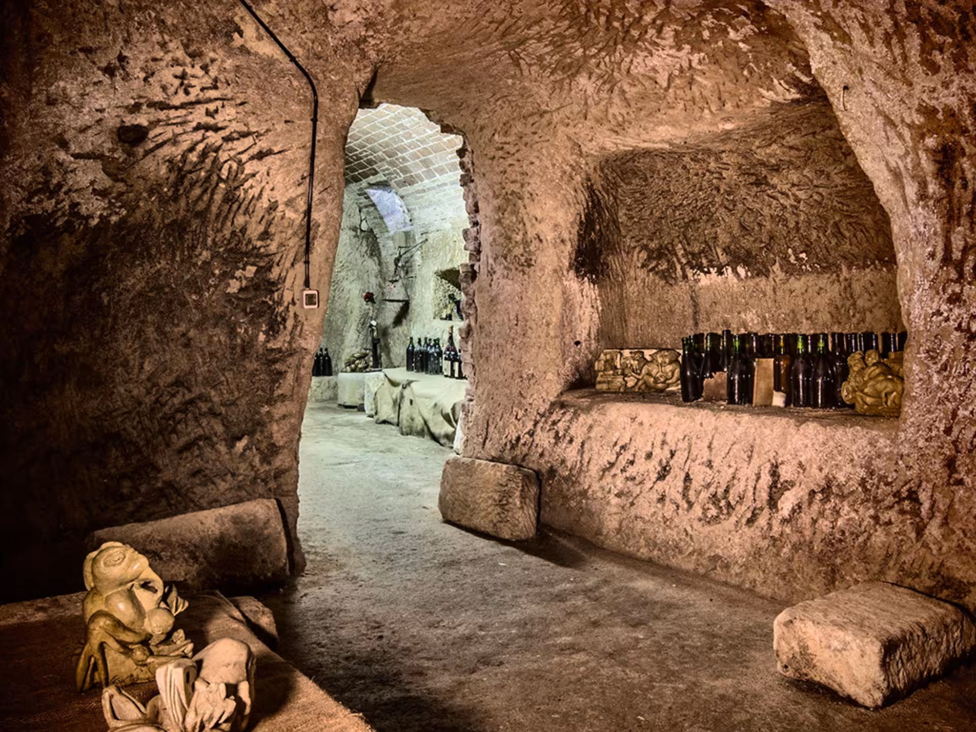Cozy cave room near Asti with wine bottles on stone shelves, offering a unique setting for tasting experiences.