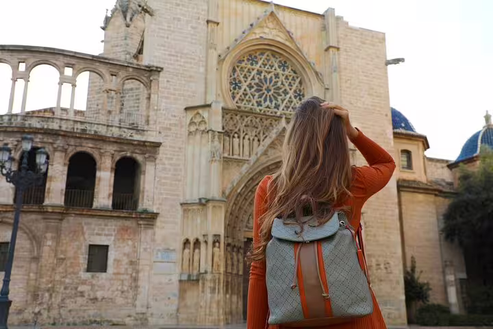 A woman with a backpack admires the historic architecture of Valencia Cathedral during a private half-day tour with local tasting.