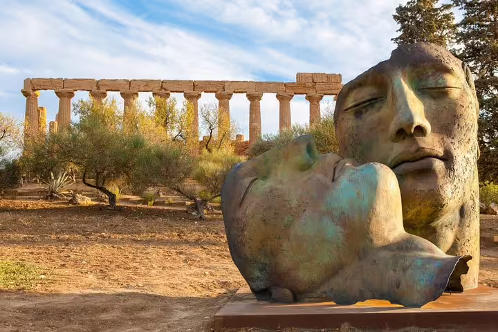 Modern bronze face sculptures set before ancient Greek temple ruins in Agrigento’s Valley of the Temples, Sicily private tour