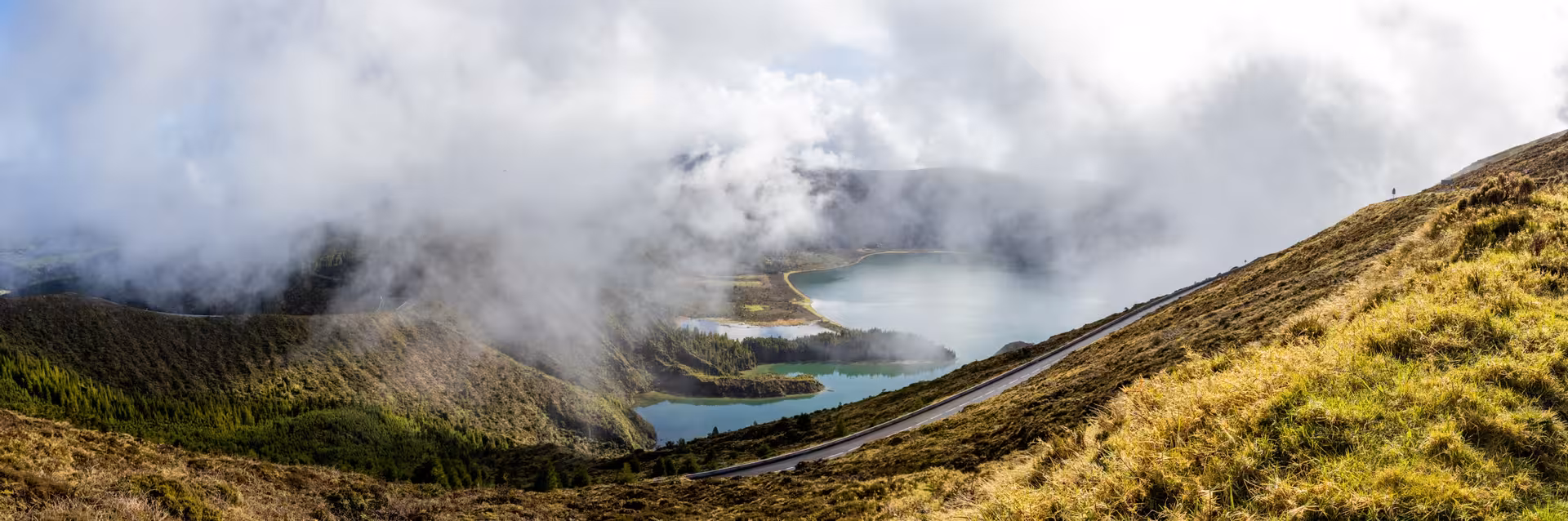 Scenic van tour view of Lagoa do Fogo crater lake with clouds and winding road, São Miguel Azores