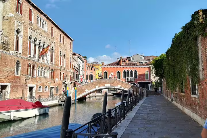 Sunlit bridge over a tranquil Dorsoduro canal lined with historic brick palaces and boats on the Accademia Gallery walking tour