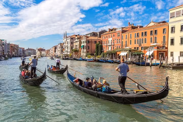 Gondolas glide along the Grand Canal under a blue sky during a Venice walking tour and gondola ride experience.