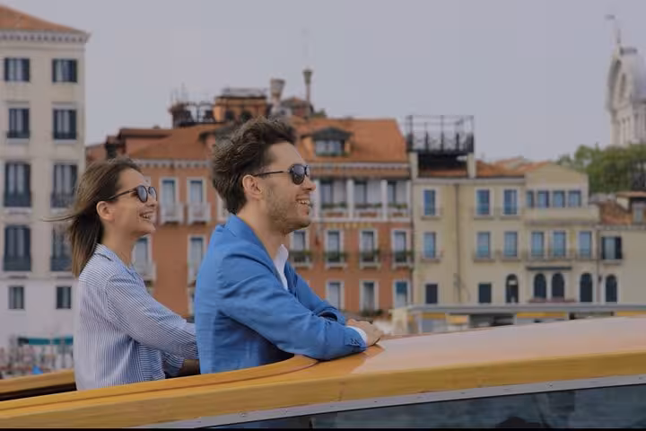 Smiling couple enjoying a water taxi ride through Venice with historic architecture view en route to Treviso Airport.
