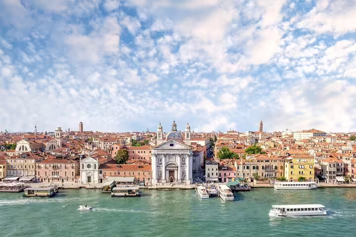 Panoramic view of Venice waterfront with historic basilica, terracotta rooftops and vaporetto boats on a private canal tour
