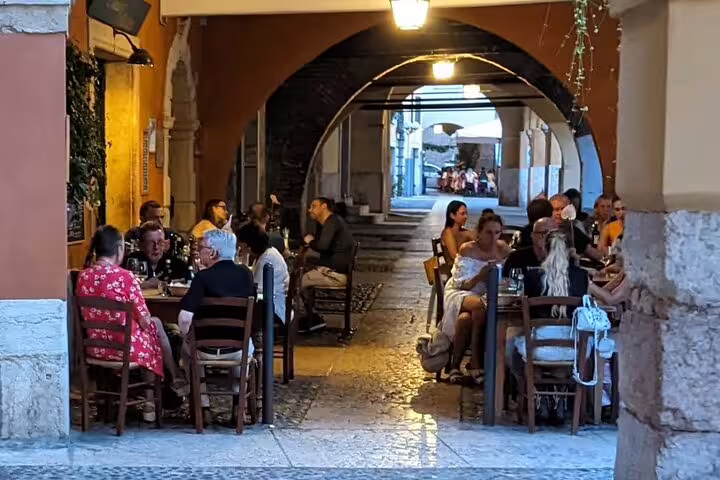 Evening scene under Verona’s arches with outdoor dining, a stop on a guided walking tour of landmarks