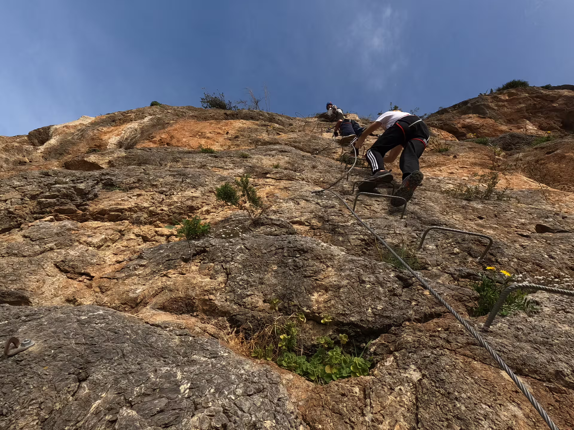 Adventurers scaling a steep cliff with safety gear on the Via Ferrata route in Casares, offering stunning views.