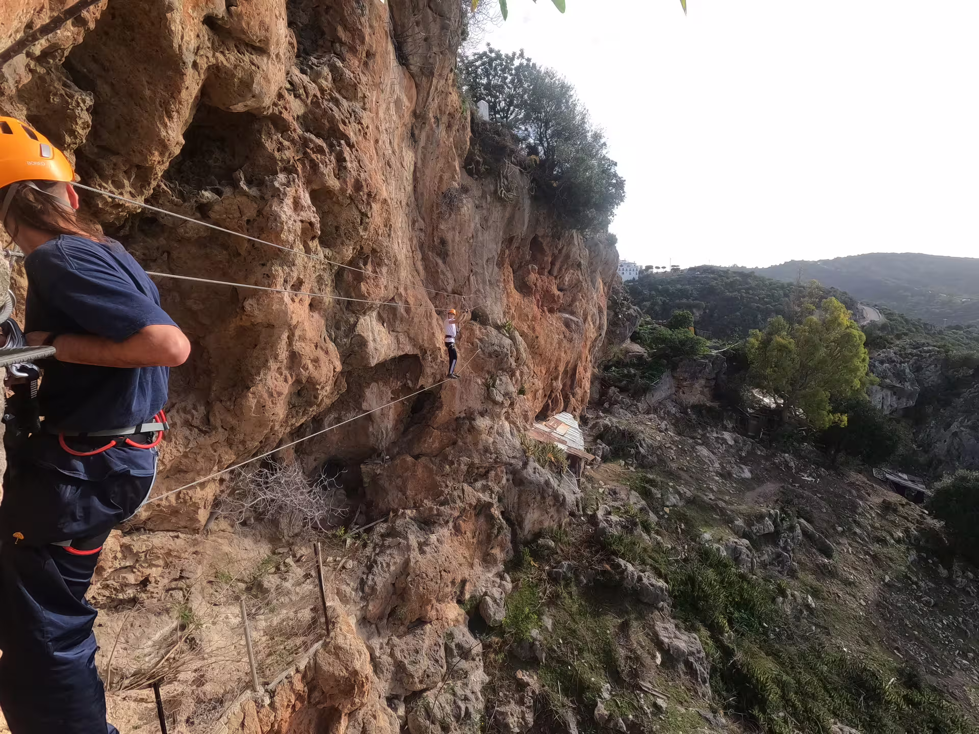 Participants tackle a daring Via Ferrata path along a steep cliff in Casares, surrounded by lush landscapes and clear skies.