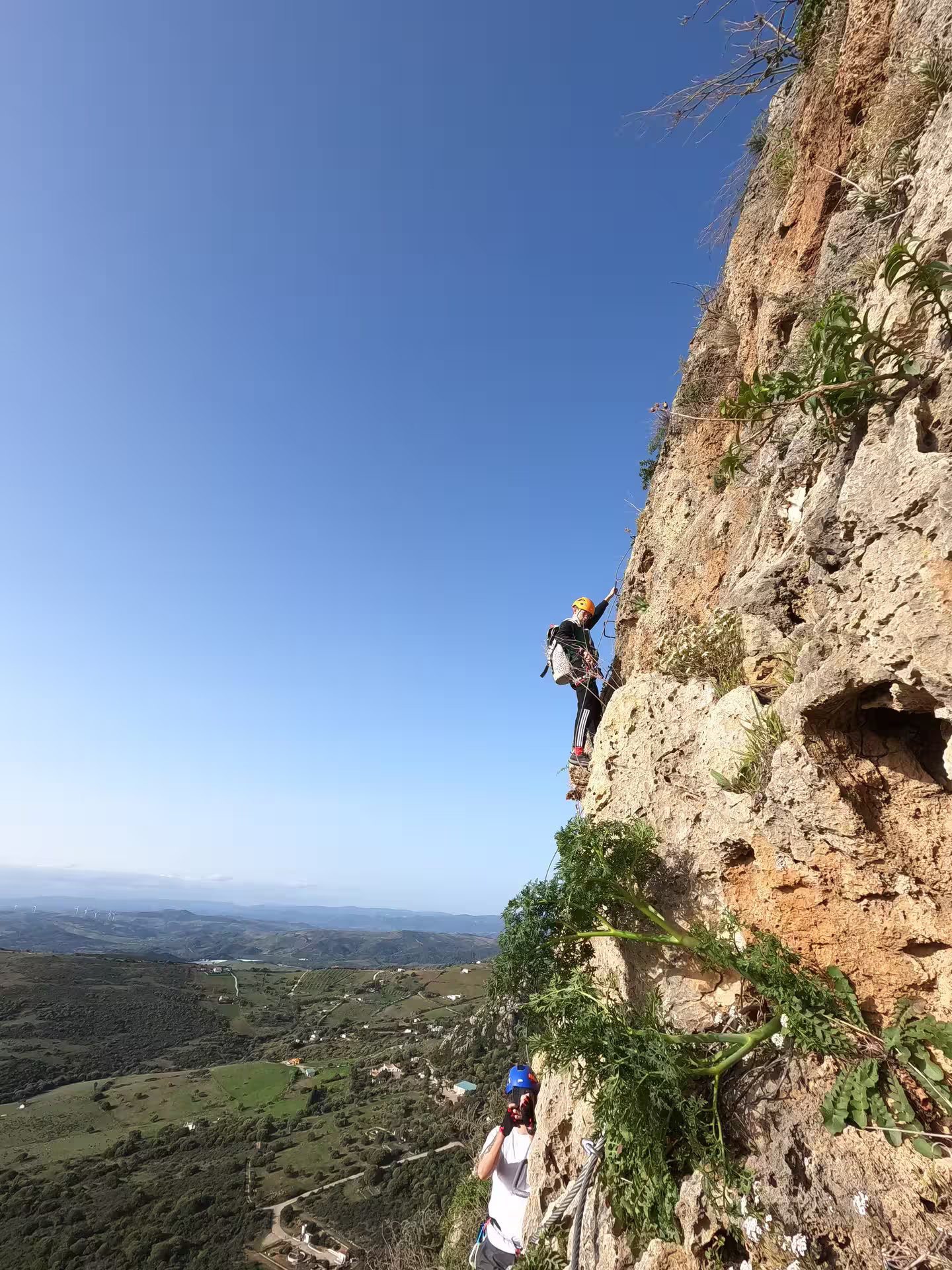 Adventurer climbing steep Via Ferrata in Casares with breathtaking panoramic views of lush green landscapes.
