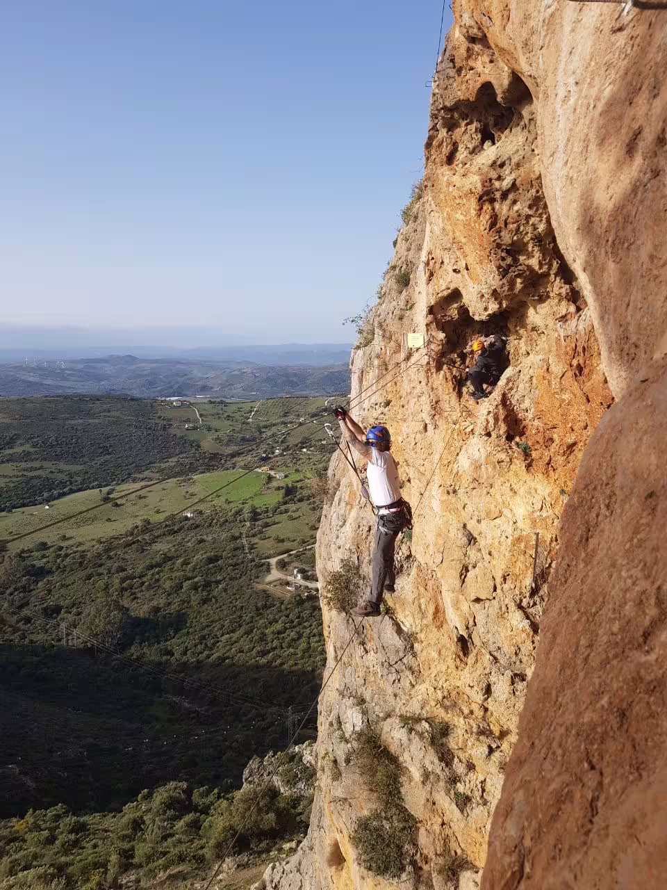 Climbers equipped with helmets and harnesses scaling a rocky path on the Via Ferrata in Casares with scenic views.