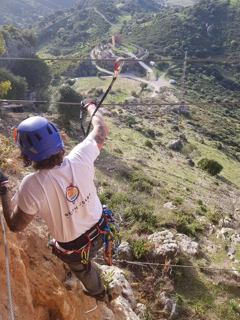 Adventurer climbing Via Ferrata in Casares with safety gear, overlooking stunning mountainous landscape and ancient ruins.