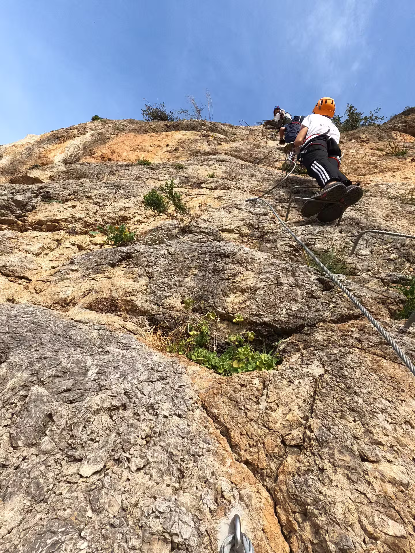 Climbers navigate a rocky Via Ferrata route in Casares, Spain, under a clear blue sky, showcasing a thrilling adventure.