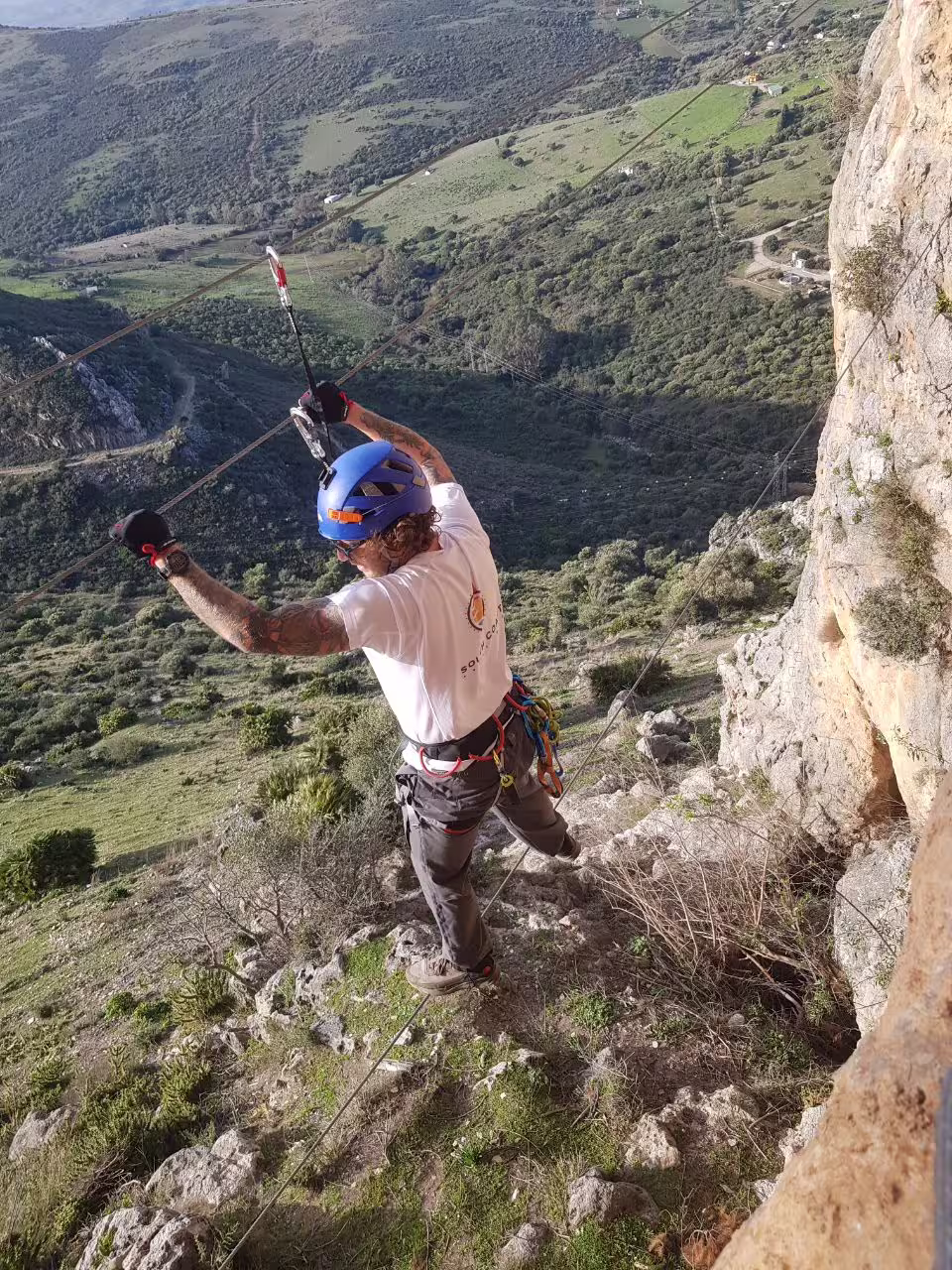 Adventurer crossing a suspension wire on a Via Ferrata route in Casares, enjoying breathtaking mountain views.