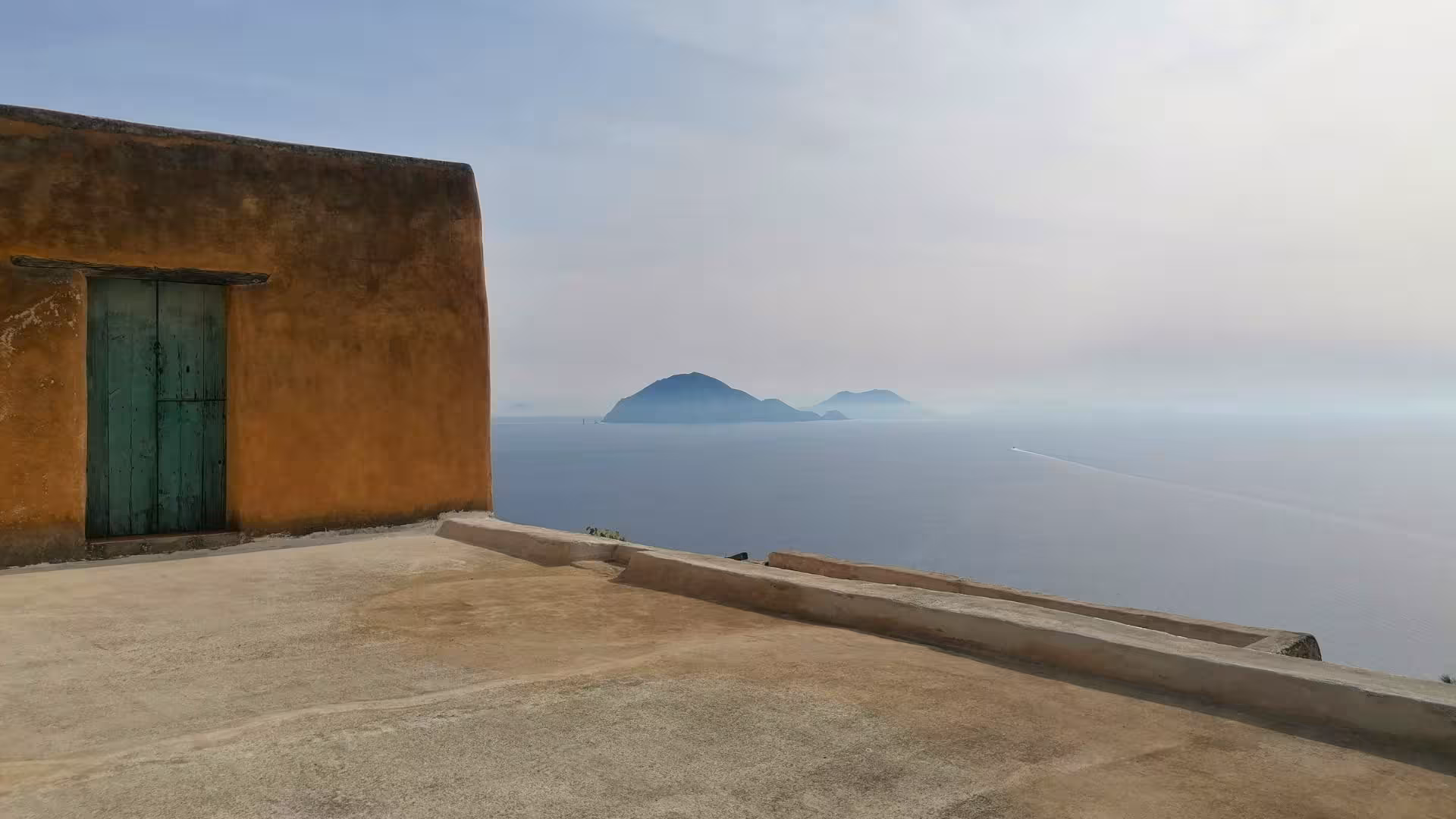 Breathtaking view of distant islands from a rustic terrace, showcasing the serene beauty of the Aeolian Islands tour.