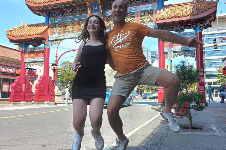 Travelers jump for a photo at Victoria Chinatown Gate on a scavenger hunt city highlights walking tour