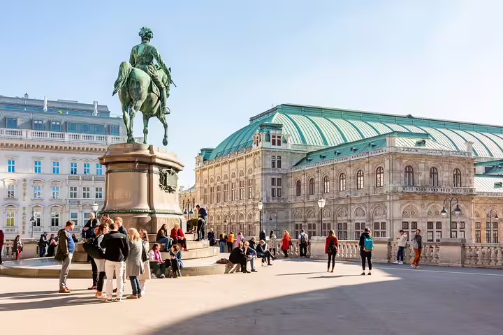 Tourists gather around a historic statue near Vienna's grand opera house, highlighting the city's architectural and cultural allure.
