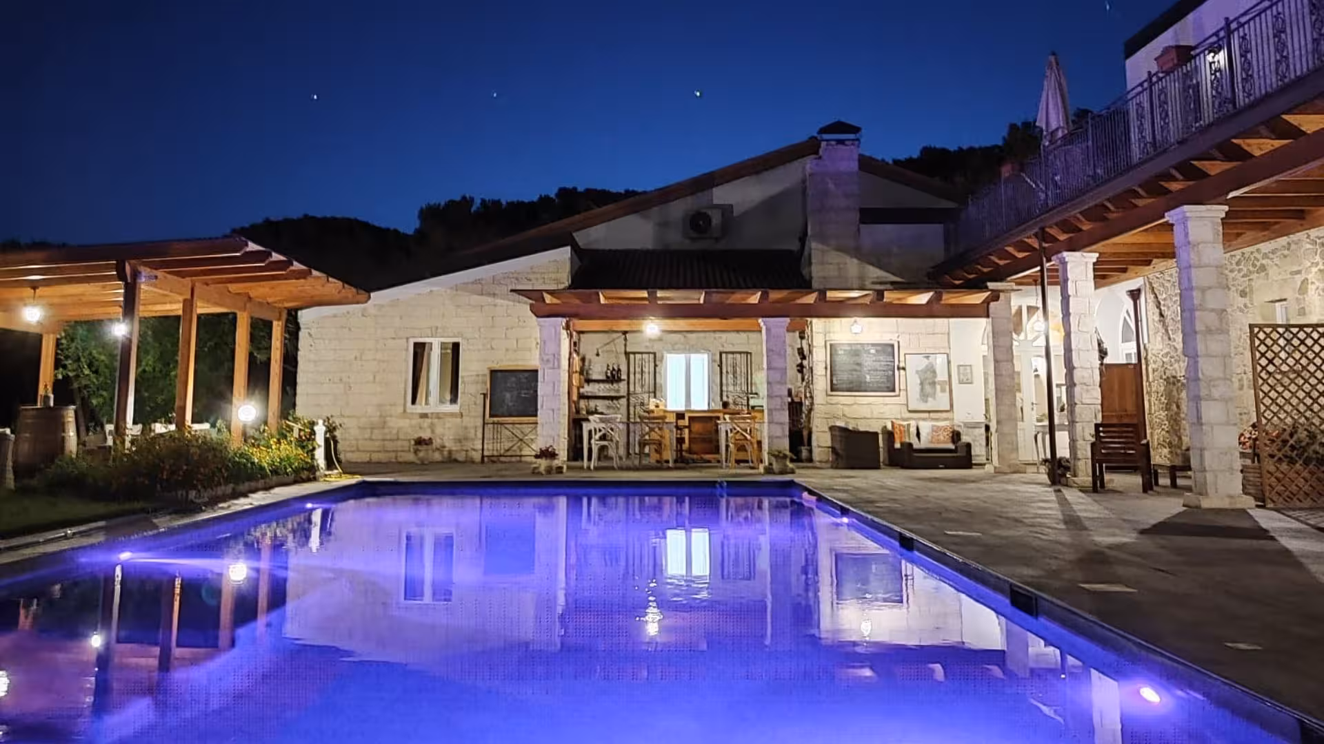 Elegant evening view of villa with illuminated poolside, perfect for a pizza workshop and dining under the stars.