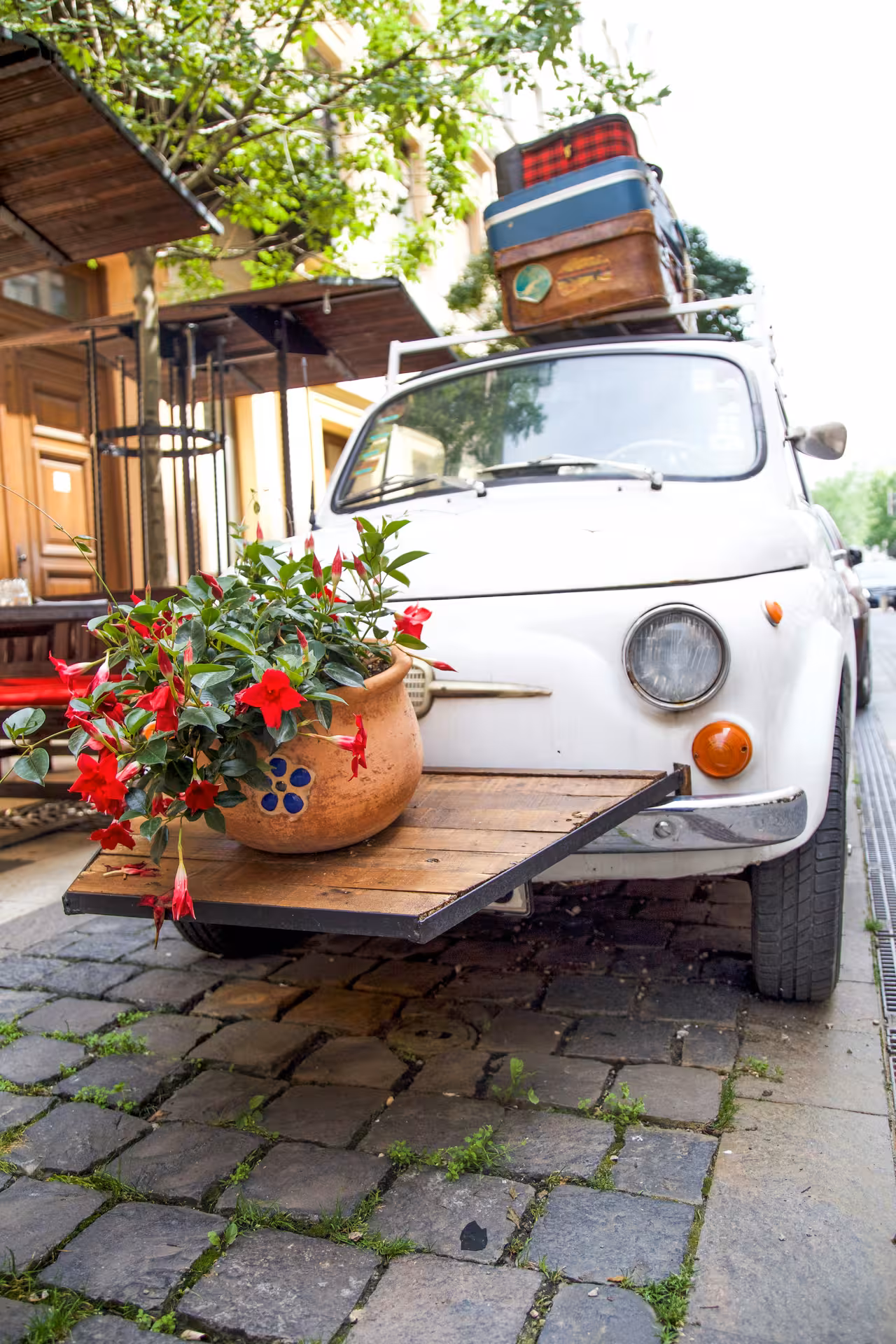 Vintage Fiat 500 with luggage and flowers on cobblestone street in Rome, perfect for a Roman Hills tour.