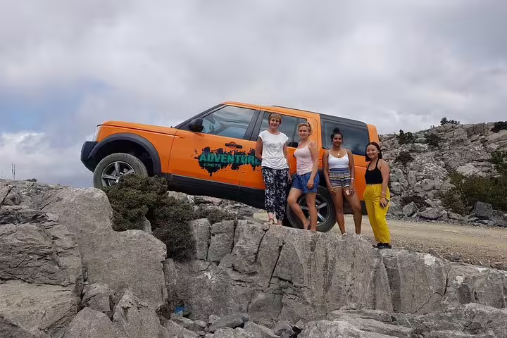 Four women standing on rocky terrain beside an Adventure-branded Land Rover during a VIP 4x4 excursion.