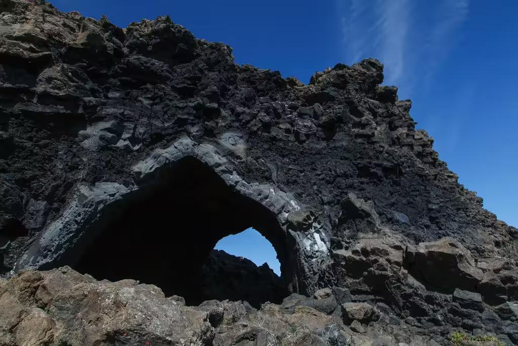 Dark volcanic rock arch formation against blue sky on Diamond Circle tour from Akureyri