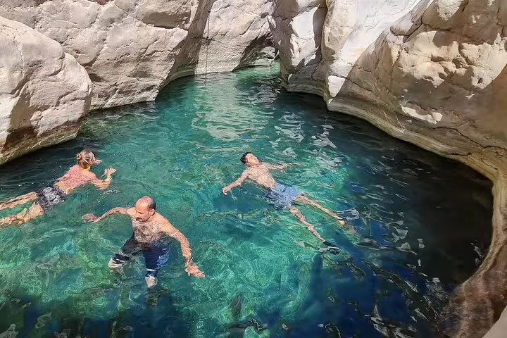 Three people enjoying a refreshing swim in the crystal-clear waters of Wadi Bani Khalid's natural pool.