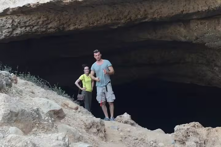 Adventurous duo standing at the entrance of a majestic cave in Wadi Shab, Oman, on a guided full-day tour.