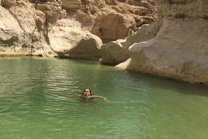 Person swimming in the clear, turquoise waters of Wadi Shab surrounded by rugged rock formations in Oman.