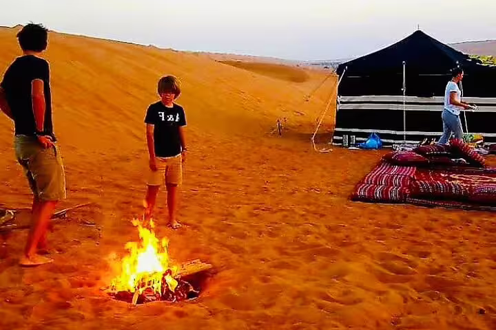 Family enjoying a campfire beside a traditional tent in the Wahiba Sands desert during a private tour from Muscat.
