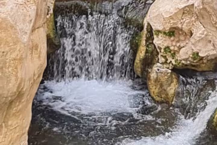 Small waterfall cascades over rocks in a serene oasis setting during the Wahiba Sands Desert camping tour from Muscat.