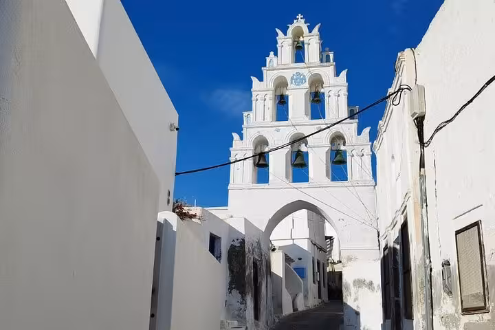 White bell tower church in Pyrgos, Santorini, framed by narrow alley on iconic highlights tour