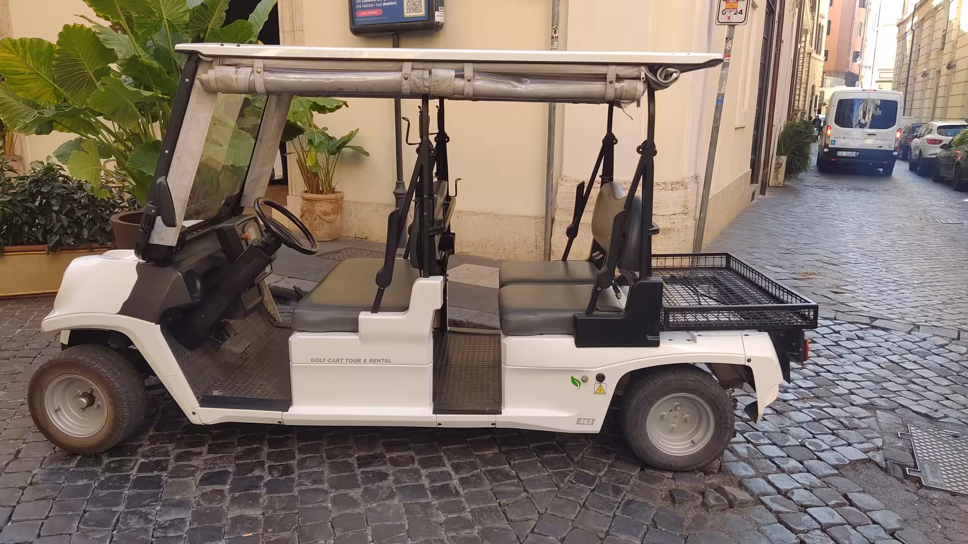 White golf cart parked on cobblestone street in Rome, ideal for exploring the city's charming alleys and attractions.