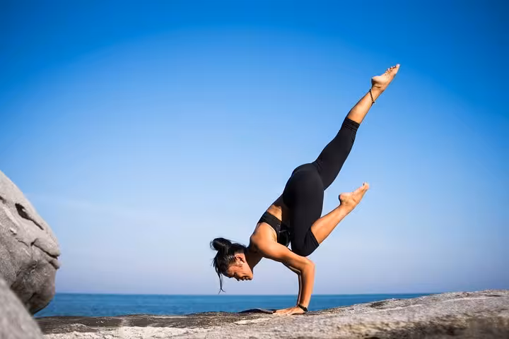 Woman practicing arm balance yoga on seaside rocks, Santorini Serenity caldera view wellness experience