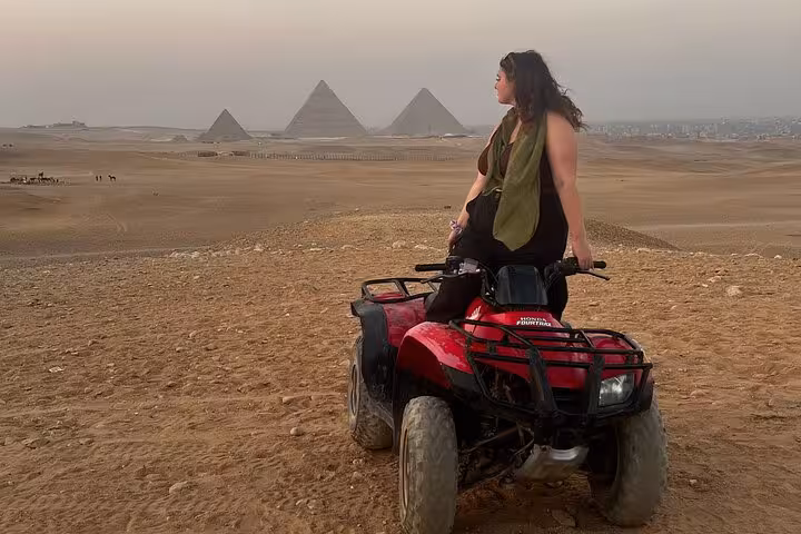 Woman on ATV overlooking the Giza Pyramids at sunset, desert quad bike trip with hotel transfers and drinks