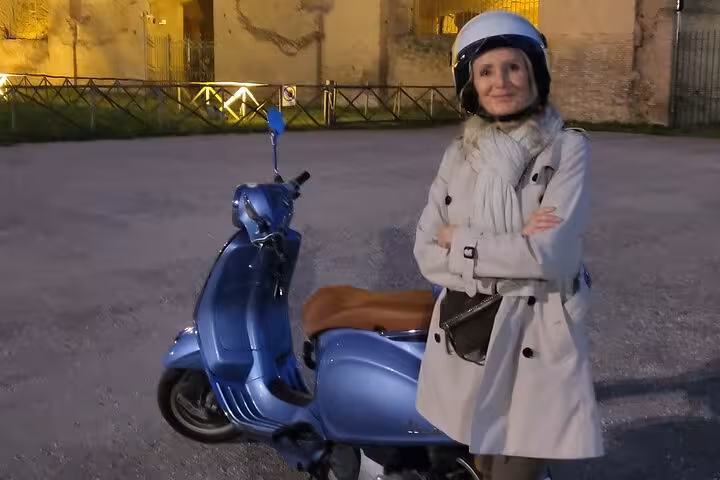 Woman in helmet poses with blue Vespa during Exclusive Private Rome by Night tour, exploring historic landmarks.