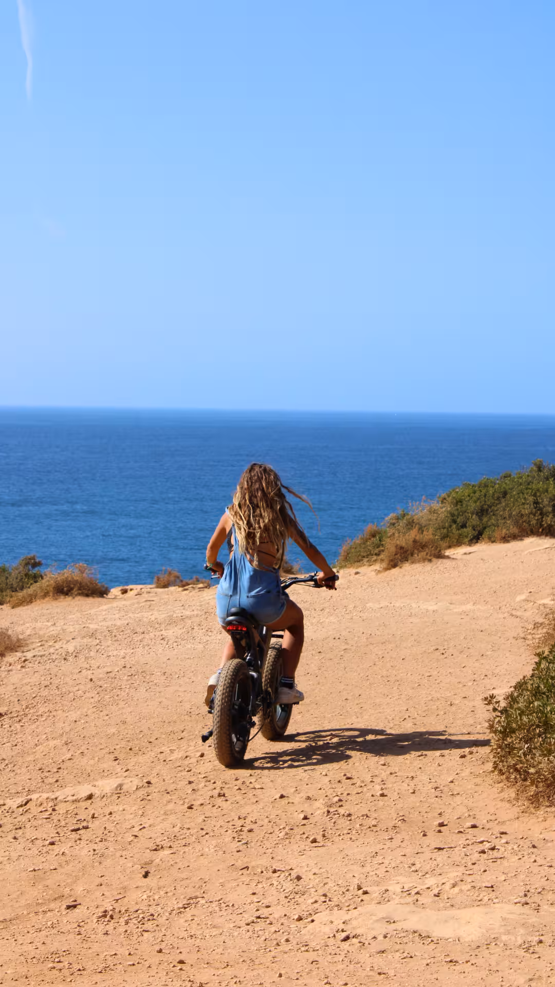 Woman rides an electric bike along a dusty Algarve cliff path overlooking the Atlantic on the Seven Hanging Valleys tour
