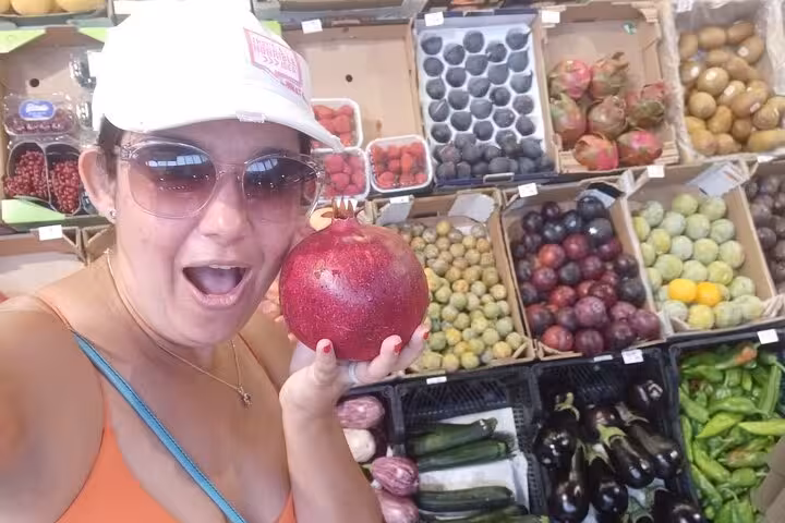 Smiling woman holding a pomegranate in Marbella market, showcasing vibrant produce on Taste of Marbella tour.