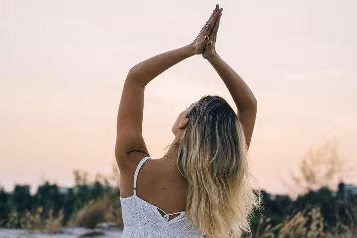 Woman stretching in prayer pose at sunset, Santorini caldera yoga retreat for calm, breathwork and flow