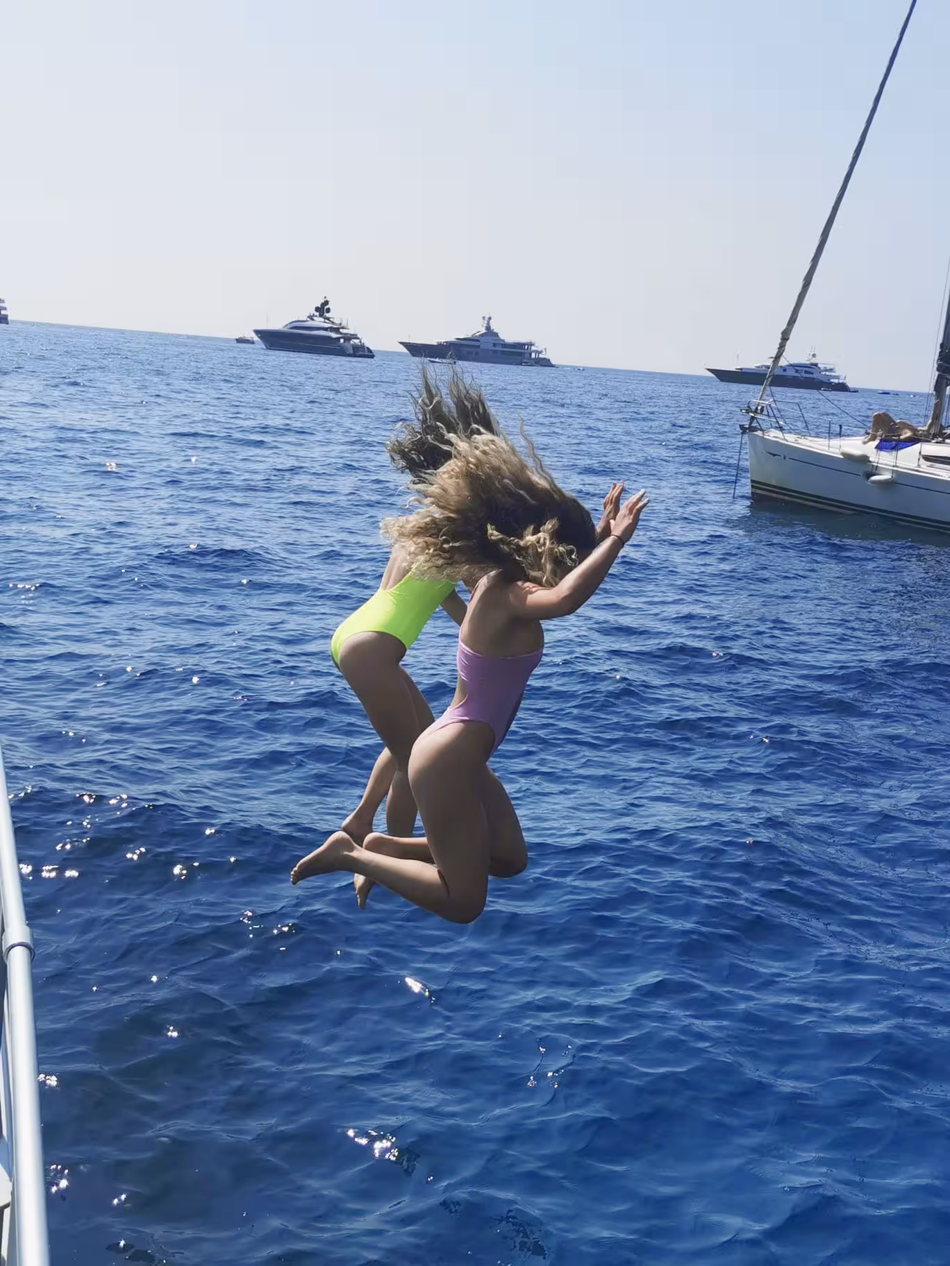 Two women in swimsuits joyfully jump into the sea during a Capri boat tour from Sorrento with limoncello.