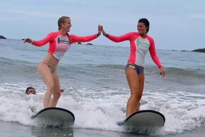Two women joyfully high-fiving while surfing waves in Manuel Antonio, showcasing the excitement of surf lessons.