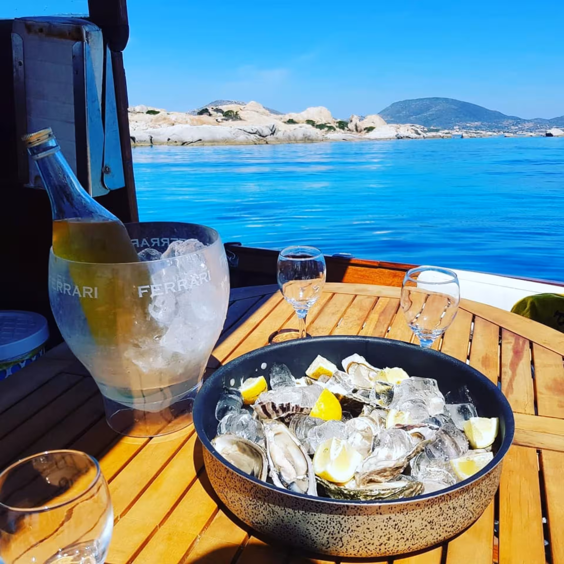 Champagne and oysters on a wooden table aboard a boat with scenic Asinara Island backdrop.